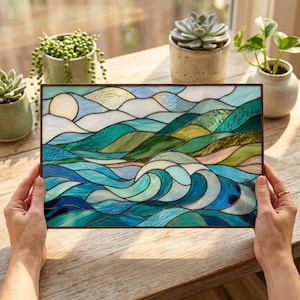May include: A rectangular stained glass panel featuring a landscape of rolling hills and ocean waves. The design uses various shades of blue, teal, and green glass pieces joined by dark metal lines, depicting a sunlit sky and a breaking wave.