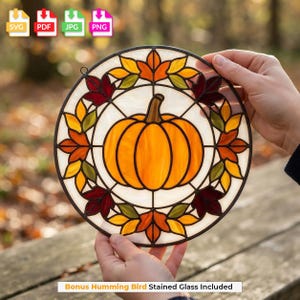 May include: A circular stained glass suncatcher featuring a central orange pumpkin surrounded by a border of autumn leaves in shades of red, orange, and green. The design is held together by dark metal lead lines, creating a decorative seasonal piece.