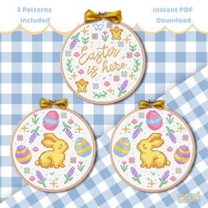 Pode incluir: Três padrões de ponto cruz em aros de madeira com temas de Páscoa. Um aro diz "Easter is here" com detalhes florais e de estrelas. Os outros dois aros apresentam ovos de Páscoa e um coelhinho amarelo. O fundo é um padrão xadrez azul e branco.