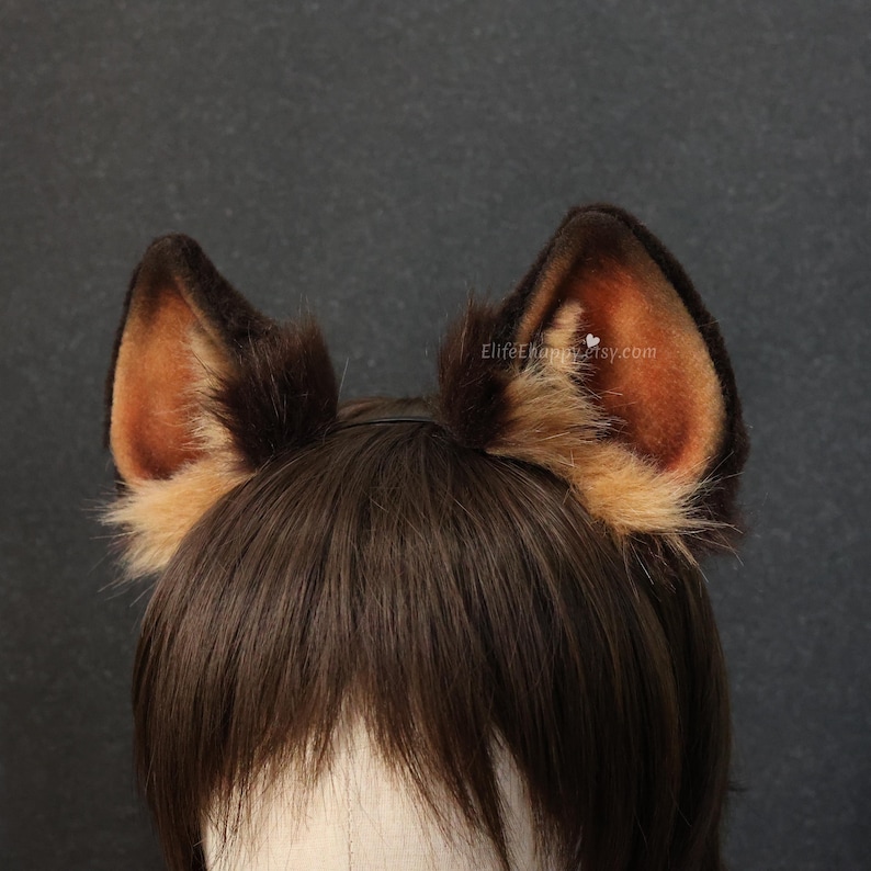 May include: A pair of brown and tan faux fur animal ears on a black headband. The ears have a dark brown exterior with tan and light brown interior. The text "ElifeKhampertsy.com" is visible on the right ear.