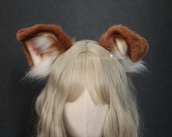 May include: A pair of plush animal ears in shades of brown and white, attached to a headband. The ears feature a soft, fuzzy texture with white fur on the inner sections and brown fur on the outer edges. The text EliteEnappy.etsy.com is visible.