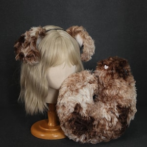 以下が含まれることがあります： 黒いヘアバンドに茶色とクリーム色のぬいぐるみ犬の耳のセットと、お揃いのふわふわの尻尾。 耳と尻尾は柔らかく、質感のある生地で作られており、コスプレやコスチュームパーティーに最適です。 マネキンの頭に展示されています。