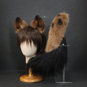 May include: A brown and black faux fur cosplay set, including a pair of ears and a tail. The ears are brown with darker tips, and the tail transitions from brown to black. The set is displayed on a mannequin head and a metal stand.