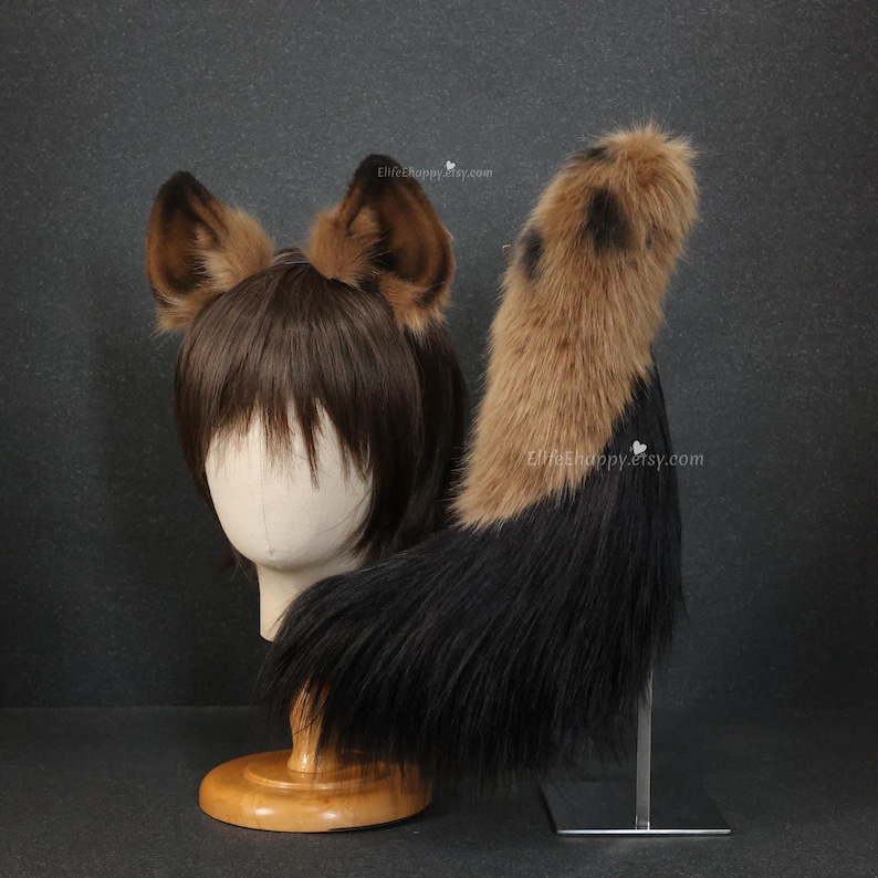 May include: A brown and black faux fur cosplay set, including a pair of ears and a tail. The ears are brown with darker tips, and the tail transitions from brown to black. The set is displayed on a mannequin head and a metal stand.