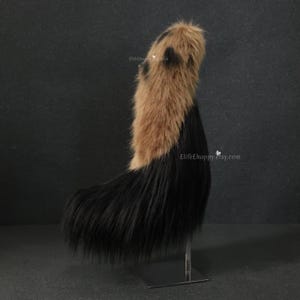 May include: A faux fur tail in a two-tone design. The top section is a light brown with dark brown spots, transitioning to a long, black, fluffy tail. The tail is displayed on a metal stand. The Etsy shop name "ElifeHappy.etsy.com" is visible.
