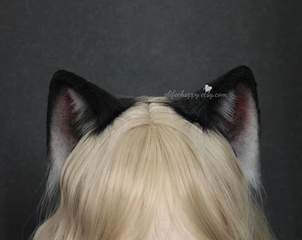 May include: Black and white faux fur cat ears with pink inner ear detail. The ears are attached to a headband and are worn on top of a blonde wig. The Etsy shop name, elifehappy.etsy.com, is visible on the right ear.