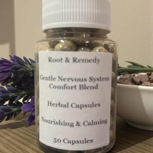 Pode incluir: Uma garrafa de plástico transparente cheia de cápsulas de ervas verdes. A garrafa tem uma tampa branca e um rótulo com o texto "Root & Remedy", "Gentle Nervous System Comfort Blend", "Herbal Capsules", "Nourishing & Calming" e "50 Capsules".