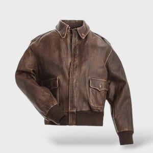 Könnte beinhalten: Braune Lederjacke im klassischen Bomberstil. Sie hat einen Kragen, zwei Vordertaschen und gerippte Bündchen und Saum. Die Jacke hat einen Reißverschluss und ein Used-Finish.