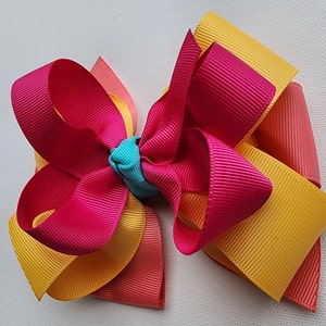 May include: A large, multi-layered bow made of pink, yellow, and orange ribbon. The bow is tied with a small turquoise ribbon in the center.