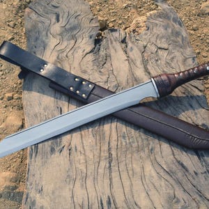 May include: A silver-bladed sword with a brown leather-wrapped handle and a matching sheath. The sword rests on a weathered wooden surface, with a black leather belt and sheath. The sword's blade is straight and has a sharp point.
