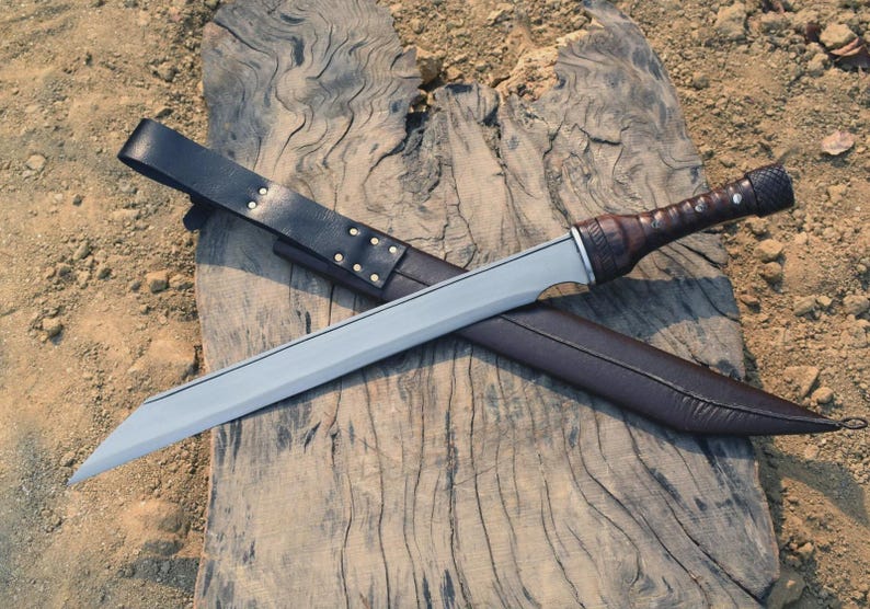 May include: A silver-bladed sword with a brown leather-wrapped handle and a matching sheath. The sword rests on a weathered wooden surface, with a black leather belt and sheath. The sword's blade is straight and has a sharp point.