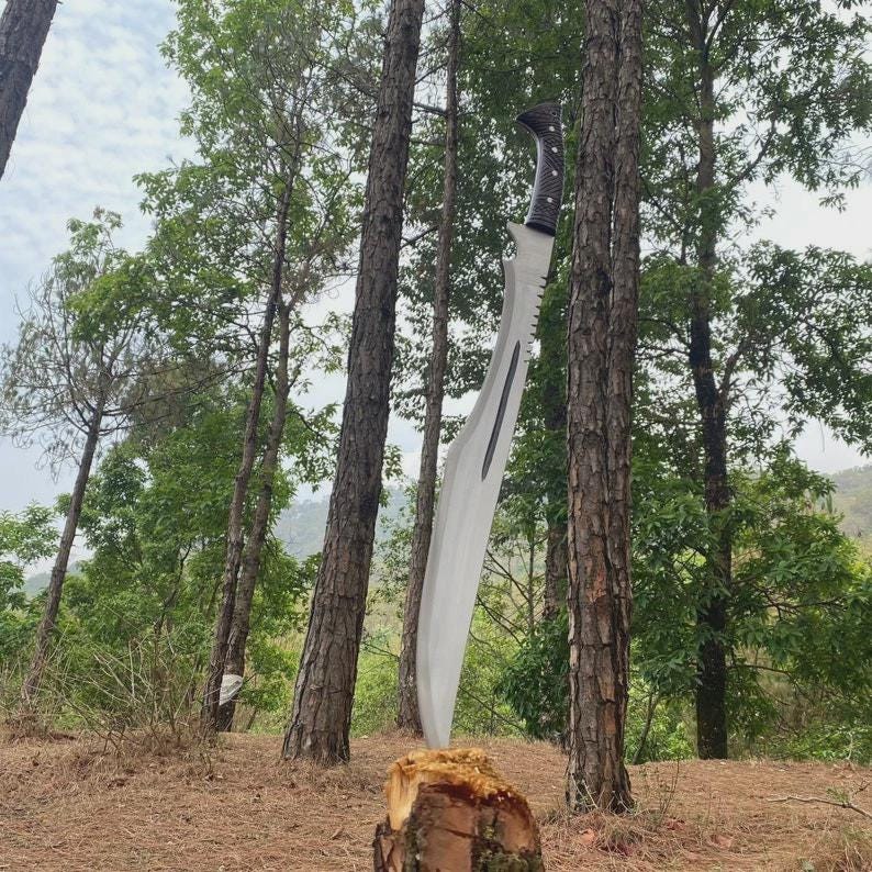 Puede incluir: Una gran machete curvada con un borde dentado y un mango oscuro y texturizado est&aacute; incrustada en un toc&oacute;n. La hoja es plateada, reflejando la luz. La escena est&aacute; ambientada en un bosque con &aacute;rboles altos y un cielo nublado.
