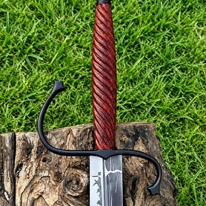 May include: A sword with a dark, matte black metal crossguard and a pommel shaped like a crown. The handle is made of reddish-brown wood with a deep, spiral-grooved texture. The blade features a distinct, dark, jagged pattern along its center.