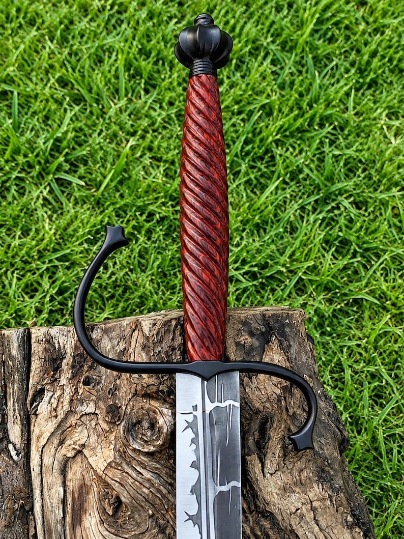 May include: A sword with a dark, matte black metal crossguard and a pommel shaped like a crown. The handle is made of reddish-brown wood with a deep, spiral-grooved texture. The blade features a distinct, dark, jagged pattern along its center.