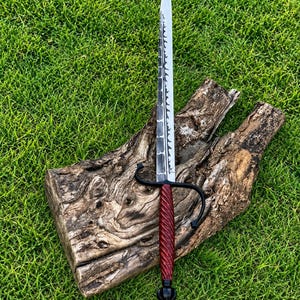 May include: A long, pointed sword with a silver-colored blade featuring a dark, textured spine. The handle is a deep red, twisted design with a black metal crossguard and a rounded black pommel at the base of the grip, creating a sharp, slender profile.
