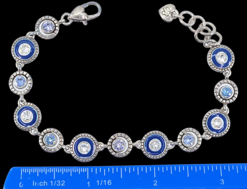 May include: Silver-toned bracelet featuring alternating blue enamel and crystal-studded circular links. The bracelet has a lobster clasp closure and a decorative heart charm. The design incorporates various shades of blue and clear crystals.