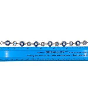 May include: Silver-toned bracelet with alternating blue and clear circular embellishments. The bracelet is approximately 7.5 inches long. The blue embellishments have a dark blue border. The bracelet is on a white background.