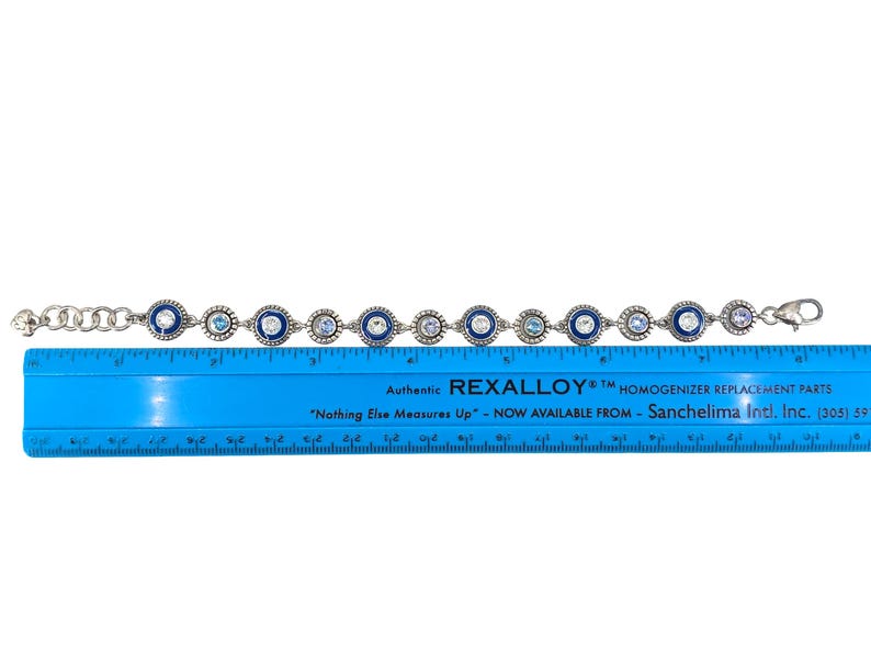 May include: Silver-toned bracelet with alternating blue and clear circular embellishments. The bracelet is approximately 7.5 inches long. The blue embellishments have a dark blue border. The bracelet is on a white background.