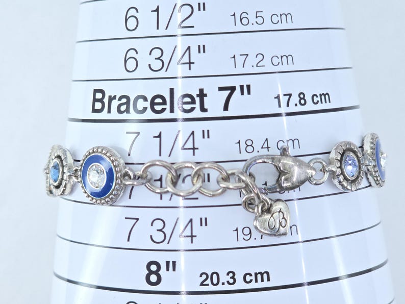 May include: Silver bracelet with blue and clear gemstone accents. The bracelet is approximately 7 inches (17.8 cm) long and features a heart-shaped charm. The bracelet is displayed on a white measuring guide.