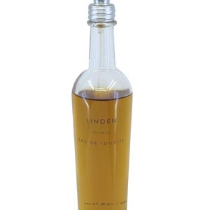 Pode incluir: Um frasco de perfume de vidro transparente com um borrifador prateado. O frasco contém um líquido castanho-dourado e apresenta o texto "LINDEN TILLEUL EAU DE TOILETTE" e a marca "fresh".