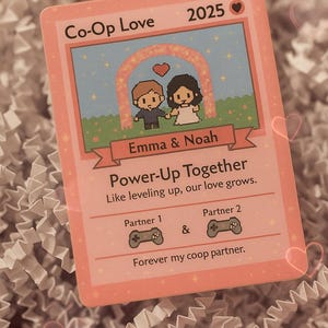 May include: A pink card with the text "Co-Op Love" and "2025". The card features pixelated illustrations of a couple under an arch and the names "Emma & Noah". It reads "Power-Up Together" and "Forever my coop partner."