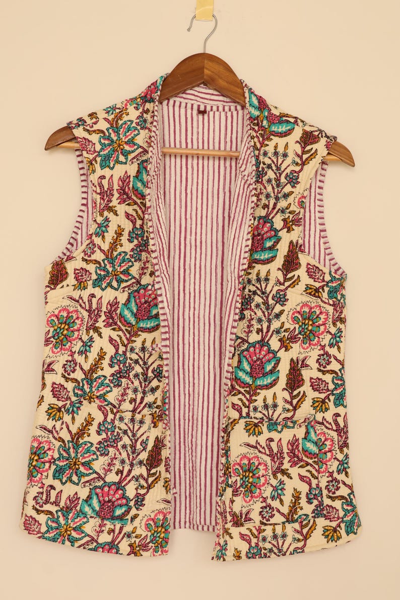 May include: A sleeveless vest with a floral pattern in teal, pink, and yellow on an off-white background. The interior lining features vertical red and white stripes. The vest is hanging on a wooden hanger.