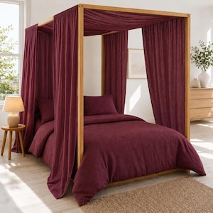 Könnte beinhalten: Ein Himmelbett aus hellem Holz, das mit tiefroten, burgunderfarbenen Stoffvorhängen drapiert ist. Das Bett ist mit einem passenden burgunderfarbenen Bettbezug und zwei Kissen bezogen, was ein einheitliches Bild innerhalb der Holzkonstruktion ergibt.