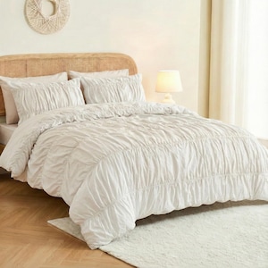 Può includere: Un letto con un piumino arricciato color crema e federe abbinate. La testiera è in rattan intrecciato. Un piccolo tappeto è ai piedi del letto. Una lampada è su un comodino.