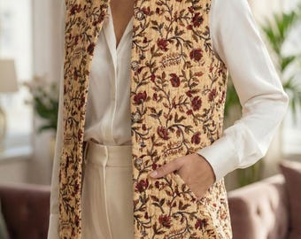 May include: A quilted vest with a floral pattern in shades of beige, burgundy, and brown. The vest has a collarless design and two pockets. The model is wearing a white blouse and cream-colored pants. The vest is a stylish layering piece.