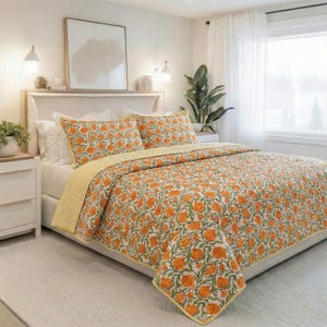 Pode incluir: Uma cama com um edredom com estampa floral e fronhas combinando. O edredom apresenta flores laranja e folhas verdes em um fundo branco. A cama é feita com lençóis brancos e uma borda amarela listrada.