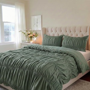Può includere: Set di biancheria da letto verde salvia con copriletto e cuscini. La biancheria da letto presenta un design arricciato, creando un aspetto strutturato. Il letto ha una testiera trapuntata e si trova in una camera da letto luminosa. L'estetica generale è morbida e invitante.