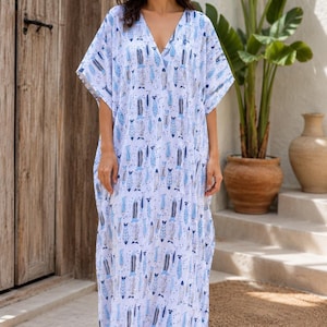 May include: A floor-length kaftan dress featuring a white base with a repeating pattern of stylised fish in shades of blue and grey. The garment has short, wide sleeves, a deep V-neckline, and a loose, flowing silhouette that reaches the ankles.