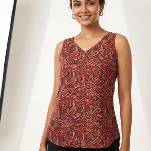 Puede incluir: Una blusa sin mangas con cuello en V, de color marr&oacute;n rojizo, adornada con un patr&oacute;n repetido de formas estilizadas en forma de hoja en tonos beige y marr&oacute;n oscuro. La blusa se combina con pantalones negros.