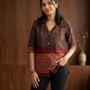 May include: A brown collared shirt with a patterned design on the lower half and sleeves. The shirt has a button-down front and three-quarter sleeves. The model is wearing black jeans.
