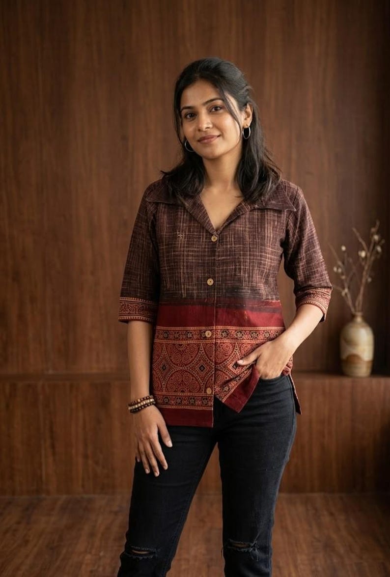 May include: A brown collared shirt with a patterned design on the lower half and sleeves. The shirt has a button-down front and three-quarter sleeves. The model is wearing black jeans.