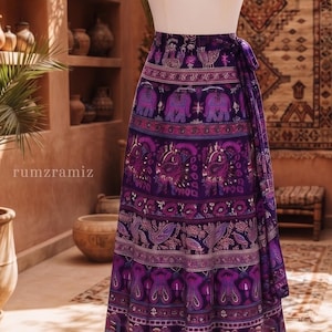 Puede incluir: Una falda cruzada de color morado hasta los pies con un patrón repetitivo de elefantes, pájaros y motivos geométricos complejos en tonos rosa, azul y blanco. La falda se muestra en un maniquí blanco e incluye el texto rumzramiz.