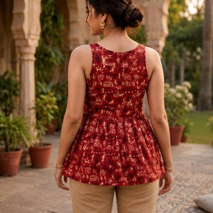 May include: A sleeveless, red top with a detailed, cream-coloured pattern. The top has a peplum design and is paired with tan-coloured trousers. The overall style is bohemian and casual.