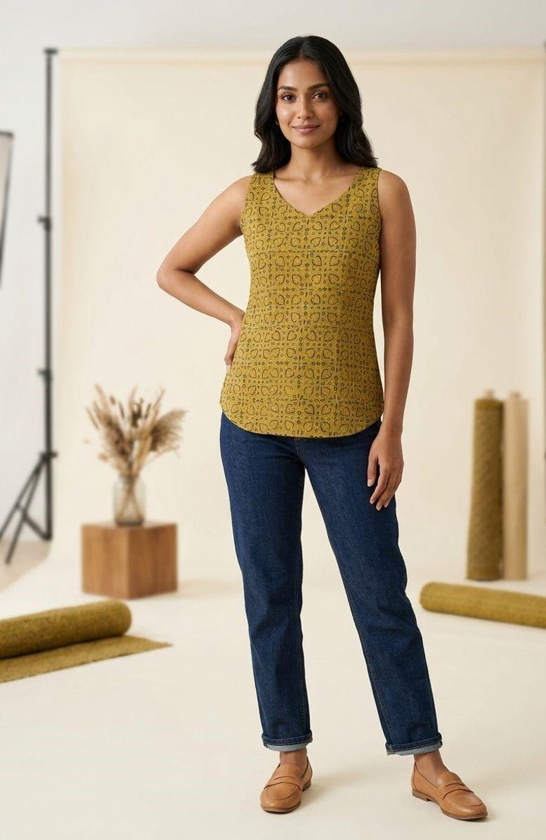 Puede incluir: Top sin mangas de color amarillo mostaza con cuello en V y un patr&oacute;n de corazones negros repetidos. El top se combina con vaqueros azul oscuro. La modelo lleva mocasines de cuero marr&oacute;n. El fondo es un estudio con tonos neutros.