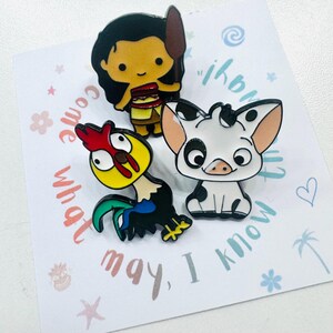 Puede incluir: Tres pines de esmalte con personajes de dibujos animados. Un pin representa a una mujer con cabello negro sosteniendo una lanza, otro un cerdo blanco con manchas negras y el tercero un gallo colorido. Los pines est&aacute;n sobre una tarjeta blanca con texto.