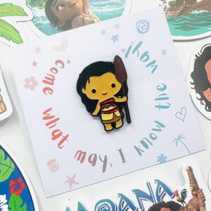 Puede incluir: Un colorido pin de esmalte con un personaje de dibujos animados con cabello negro, sosteniendo una lanza. El pin est&aacute; sobre una tarjeta blanca con el texto "Come what may, I know the way". Otros adhesivos de personajes rodean el pin.