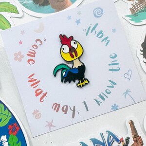 Puede incluir: Un colorido pin de esmalte con un gallo de dibujos animados con cresta roja, cabeza amarilla y plumas de cola azules y verdes. El pin est&aacute; sobre una tarjeta blanca con el texto "Come what may, I know the way!"