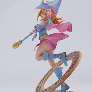 May include: A figurine of a female character in a dynamic pose, wearing a blue and pink outfit with a tall, pointed hat. She holds a staff and stands on a golden ring with a decorative pattern. The figure has blonde hair and blue boots.