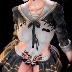 Puede incluir: Una figura que viste un top de estilo marinero gris claro con mangas negras, cuello negro y corbata negra. El top presenta el texto E.V.L. en el pecho, detalles en color cobre y una falda plisada negra con rayas horizontales doradas.