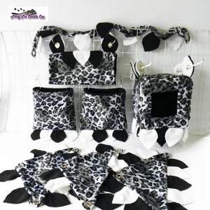 Pode incluir: Um conjunto de sete acessórios de gaiola pendurados em estampa de leopardo preto e branco para pequenos animais de estimação. O conjunto inclui uma rede, um saco pendurado, um cubo e três brinquedos pendurados.