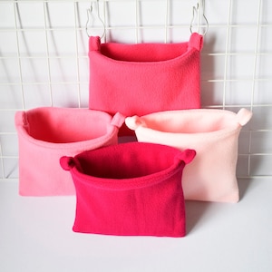 Pode incluir: Quatro camas de estimação de lã penduradas em cores rosa e vermelho. As camas são feitas de tecido macio e felpudo e têm uma forma arredondada. São perfeitas para animais pequenos como hamsters, gerbils ou ratos.