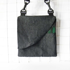 May include: A black crossbody bag with a green and black flap. The bag has an adjustable strap and a zipper closure.