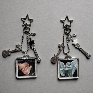 Puede incluir: Dos llaveros con arte de álbum de Deftones. Cada llavero tiene una parte superior en forma de estrella, una cadena con dijes que incluyen una guitarra, un micrófono y estrellas. Uno presenta la cara de un hombre, el otro un búho.