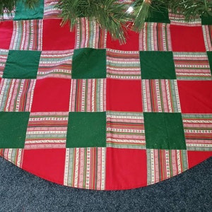 May include: A Christmas tree skirt with a patchwork design. The skirt features alternating red and green squares, with striped fabric accents in between. The skirt is made of fabric and has a semi-circular shape.