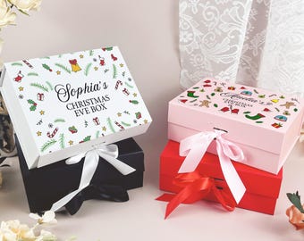May include: Gift boxes for Christmas Eve, in black, pink, and red, with white bows. The boxes are decorated with festive patterns and text that reads "Sophia's Christmas Eve Box" and "Annelia's Christmas Eve Box".