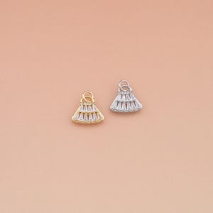 May include: Two small, pendant-style charms. One is gold-toned, the other silver-toned. Both have a tiered, skirt-like shape with clear, rectangular stones. Each charm has a small loop at the top for attaching to a chain or bracelet.